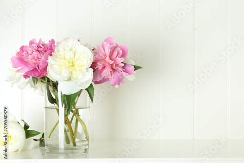 Bouquet of beautiful peonies in vase on white table. Space for text