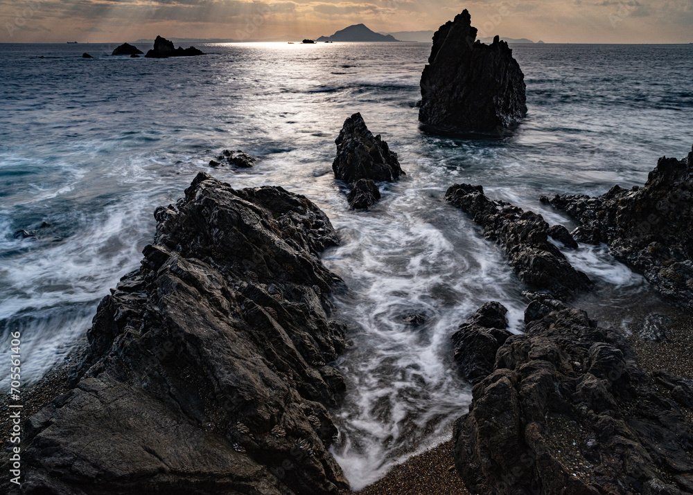 Obraz premium 夕暮れの海で岩場に打ち寄せる波