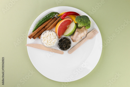 Metabolism. Plate with different food products and wooden cutlery on pale green background, top view photo