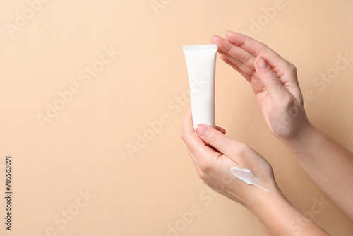 Woman with tube of hand cream on beige background, closeup. Space for text
