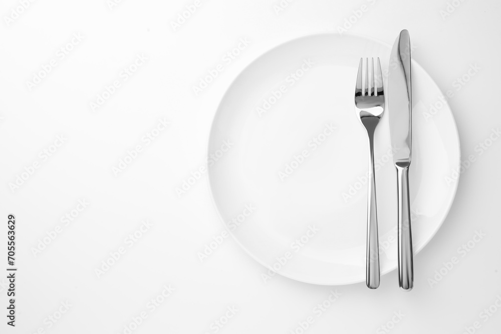 Plate, fork and knife on white background, top view. Space for text