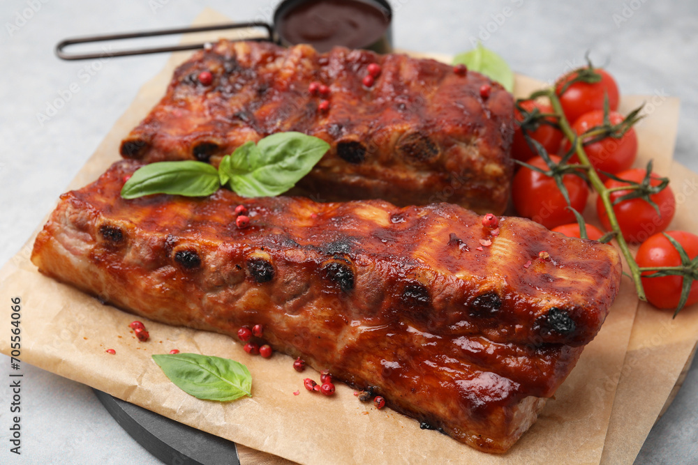 Tasty roasted pork ribs served with sauce, basil and tomatoes on grey table, closeup Tasty roasted pork ribs served with sauce, basil and tomatoes on grey table, closeup