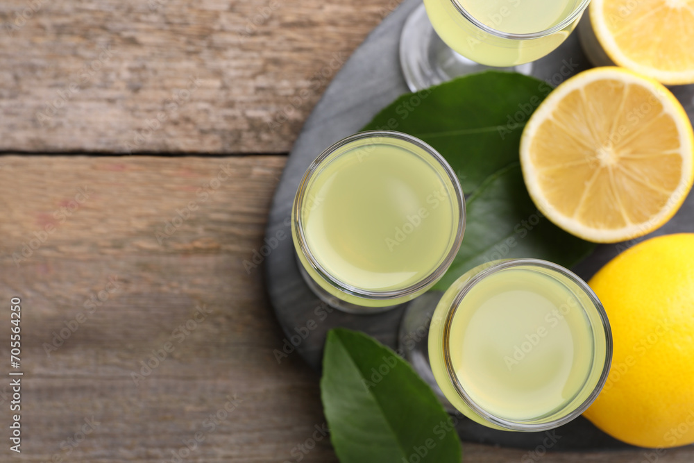 Tasty limoncello liqueur, lemons and green leaves on wooden table, top view. Space for text Tasty limoncello liqueur, lemons and green leaves on wooden table, top view. Space for text