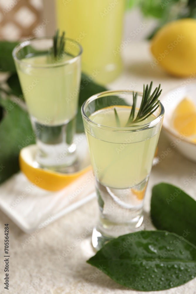 Tasty limoncello liqueur and green leaves on light textured table, closeup