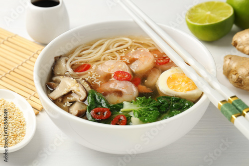 Tasty ramen with shrimps in bowl and chopsticks on white table, closeup