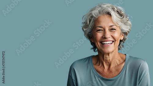 A joyous senior woman with silver hair laughing heartily, her happiness radiating in the warm light against a soft blue background photo