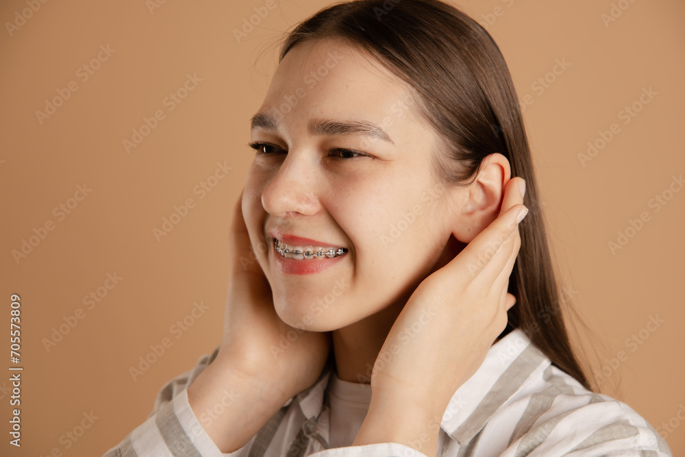 smiling woman with braces enjoy life, straightens hair with her hands on studio beige background smiling woman with braces enjoy life, straightens hair with her hands on studio beige background
