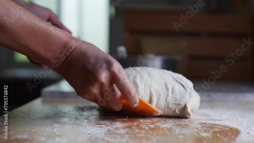 Freshly risen ball of sticky dough being shaped using orange scraping tool on wooden kitchen tabletop, filmed as close up in slow motion style photo