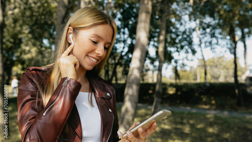 Young caucasian girl with wireless headphones in the park using tablet, phone and smiling