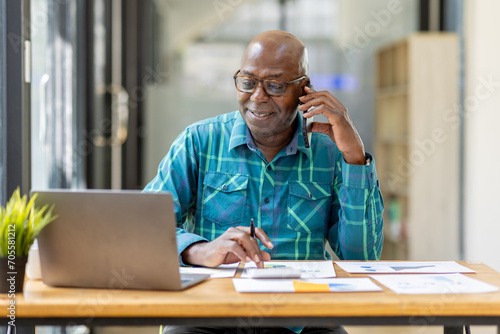 Portrait of Senior African man sitting on laptop at the home office and having a phone conversation with the insurance company. photo