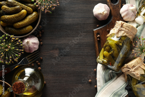 Canned cucumbers in a jar, with ingredients on a dark table.