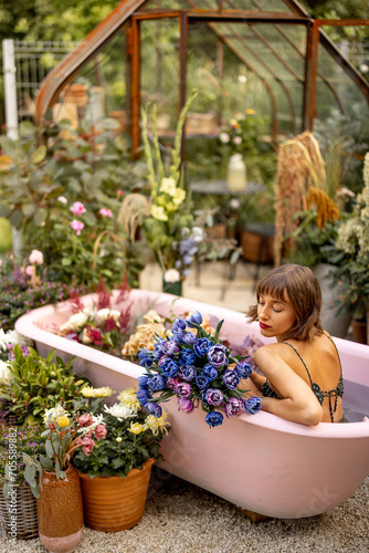Woman lying in pink bathtub with lots of flowers in garden outdoors. Concept of beauty, bizarre and flower therapy