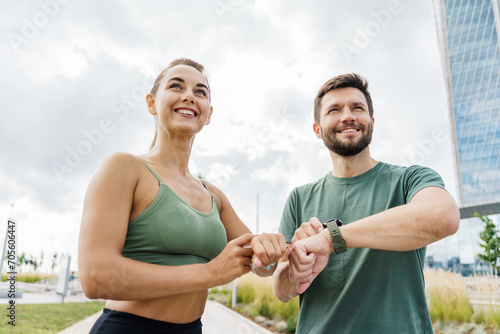 Smiling couple checking fitness progress on smartwatch after workout, urban park.