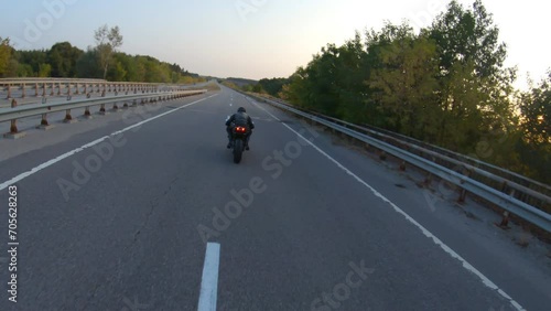 Follow to biker riding on modern sport motorbike on country road at sunset. Motorcyclist racing his motorcycle at highway. Guy driving bike during trip. Concept of journey and freedom. Aerial shot