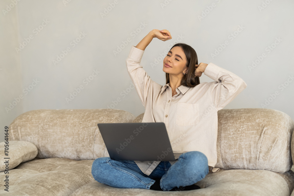 Business woman wearing white shirt sitting on sofa with laptop raising her arms above her head stretching Business woman wearing white shirt sitting on sofa with laptop raising her arms above her head stretching