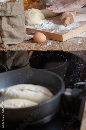 Women hands roll out dough in frying pan foreground ....