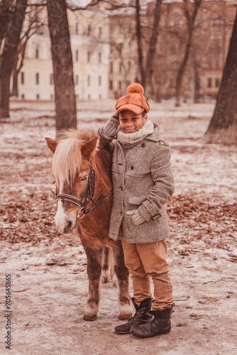 boy adjusts his hat while leaning on the pony and looking at the camera © Anna