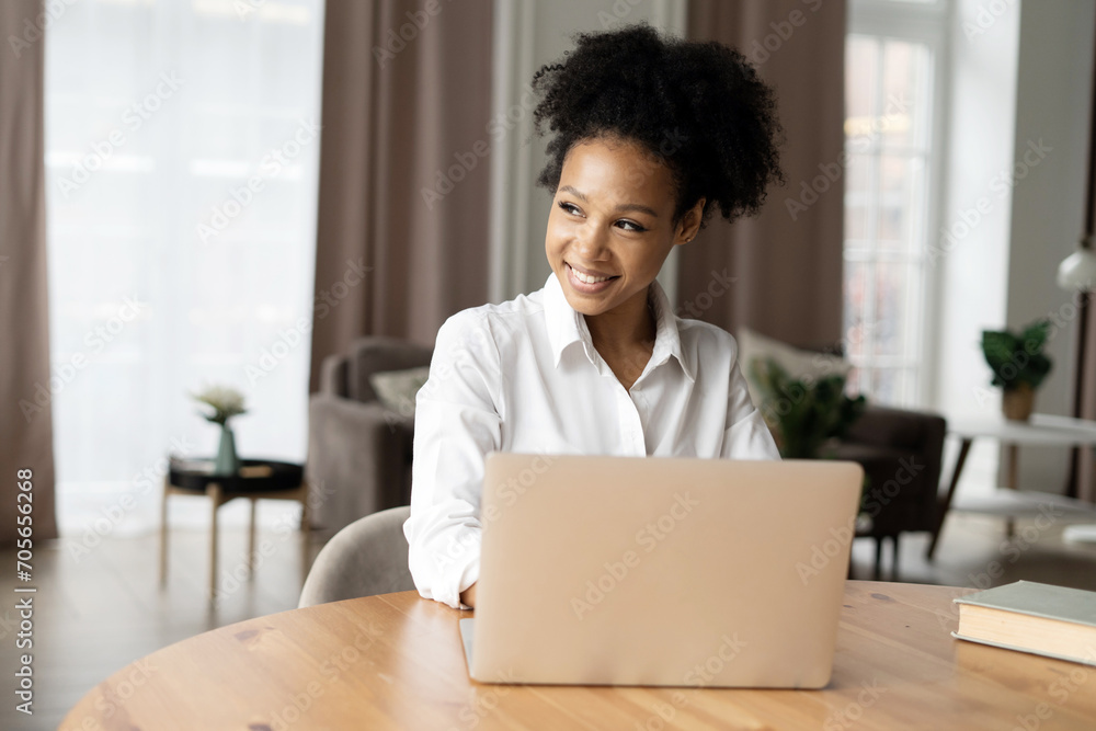 Joyful woman working on laptop with a bright smile, feeling accomplished in a cozy home setting. Joyful woman working on laptop with a bright smile, feeling accomplished in a cozy home setting.
