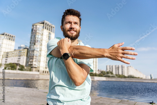 Active man performing a stretch routine along a river promenade with urban skyline.
