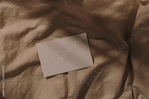 Blank paper sheet card with mockup copy space on crumpled beige bed blanket with soft warm sunlight shadows. Flat lay, top view aesthetic minimal brand template photo
