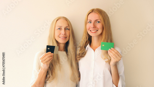 Portrait of happy smiling caucasian middle aged mother or sister and adult daughter holding plastic credit bank card together on studio background