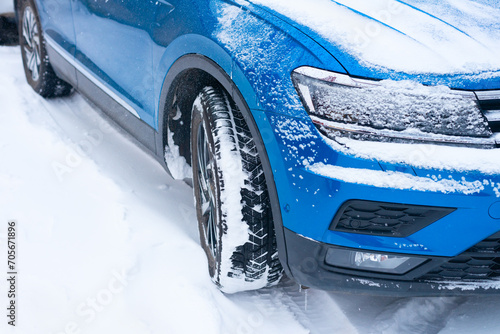 Three-quarter view of the front of a blue modern car standing on a snow-covered road.