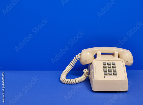 Beige retro phone with gray buttons on a blue background. Copy space for text.