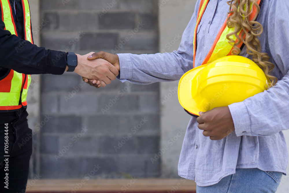 Two individuals shaking hands in front of a construction site as a gesture of agreement and partnership. Two individuals shaking hands in front of a construction site as a gesture of agreement and partnership.