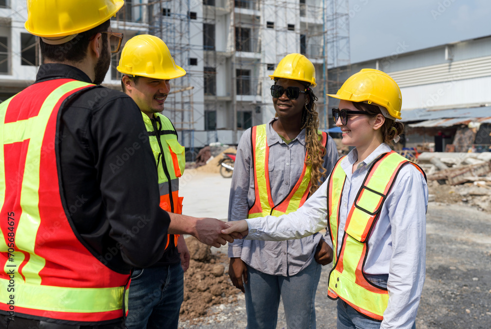 Four construction workers celebrating with a handshake in front of an active construction site. Four construction workers celebrating with a handshake in front of an active construction site.
