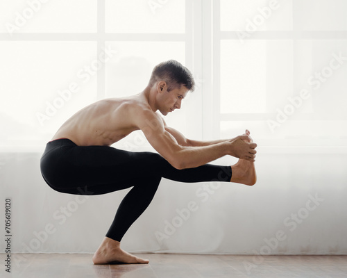 Muscular flexible athletic man doing yoga asana at home near big window, Healthy young man engages in home yoga stretch pose.