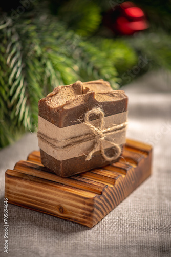 Fragrant brown piece of natural soap on an organic wooden soap dish against the background of the green branches of the Christmas tree