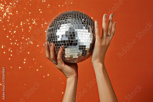 Women's hands holding disco ball on red background with gliters. Season's greetings concept. Flat lay and copy space
