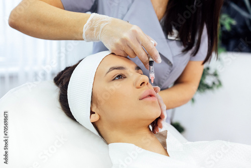 Female cosmetologist in transparent gloves makes an injection in the lower jaw of her client