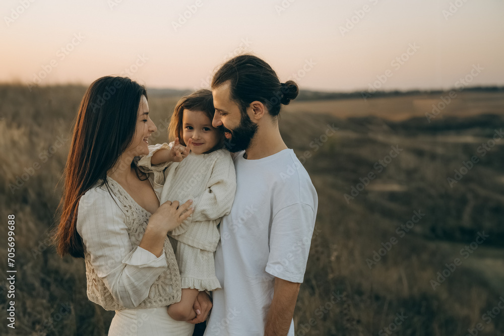 Happy family strolling in nature all together. Joyful mother, bearded father and little daughter walking on the field, noise effect Happy family strolling in nature all together. Joyful mother, bearded father and little daughter walking on the field, noise effect