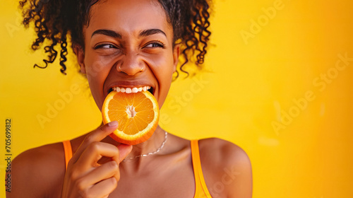 Attractive and joyful young female eat fresh orange isolated on yellow background