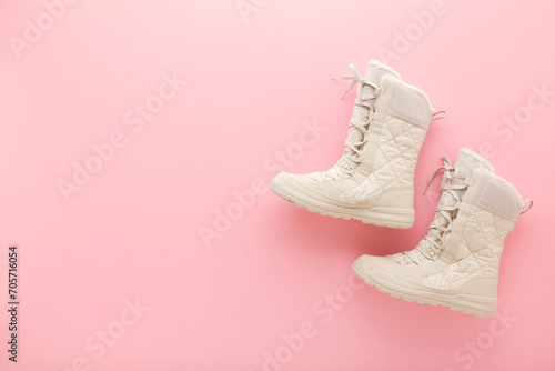New beige warm winter boots with shoelace on light pink table background. Pastel color. Female footwear. Closeup. Top down view.