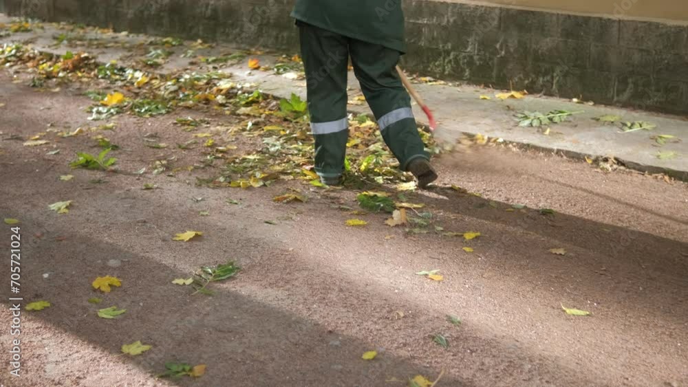 Caucasian women janitor in working uniform raking dry fall foliage at city park. Autumn garden works. Close up. Caucasian women janitor in working uniform raking dry fall foliage at city park. Autumn garden works. Close up.