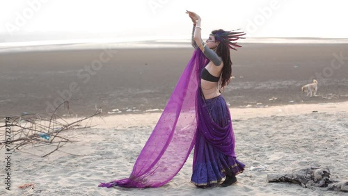 Delightful young dancer inpurple Indian national costume with ornaments, dances on seashore. 