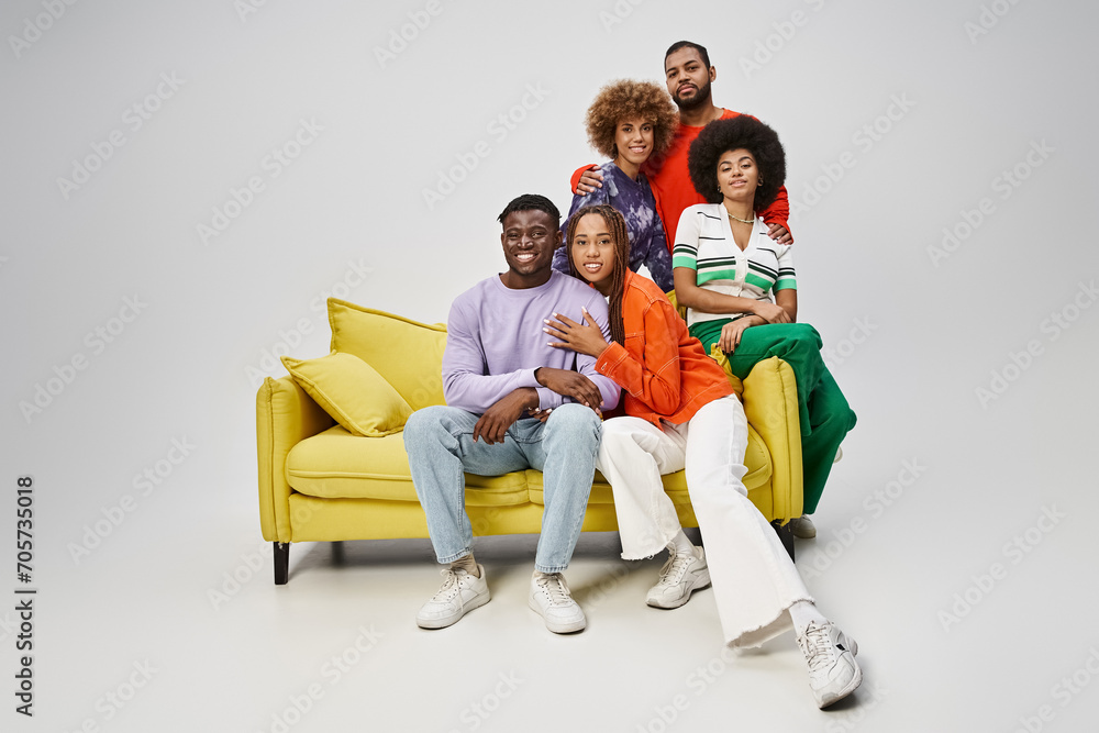 happy african american people in bright casual wear sitting together on yellow couch on grey