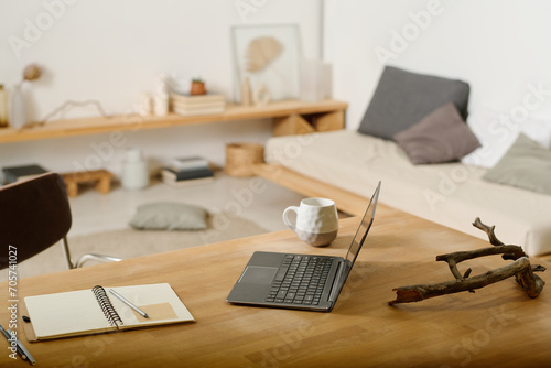 Workplace with laptop, open notepad with pencils and pen, cup of coffee or tea and decorative snag or driftwood on wooden table