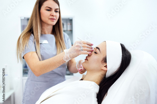 Beauty injections. Female cosmetologist in transparent gloves makes an injection in the lower jaw of her client. Treatment with hyaluronic acid. Introduction of liquid into the skin of woman.