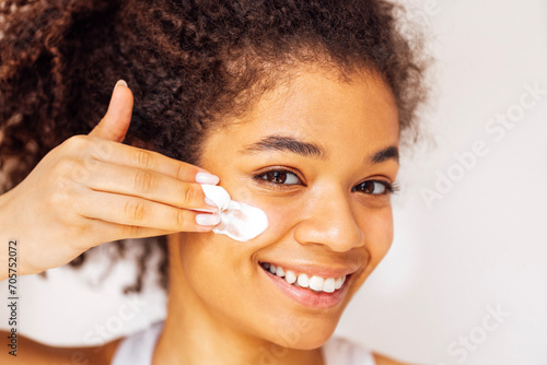 Close up beauty portrait of laughing african with wavy hair and beautiful smile applying white cream on her cheeks