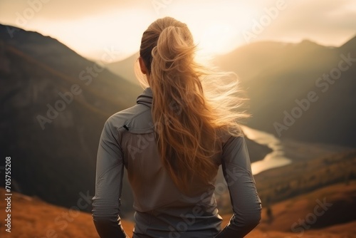  the back of a woman's head as she stands in a field with mountains in the background and a body of water in the foreground with a body of water in the foreground.