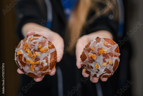 Dwa apetyczne pączki z dżemem, lukrem I skórką pomarańczową trzymane w kobiecych dłoniach 