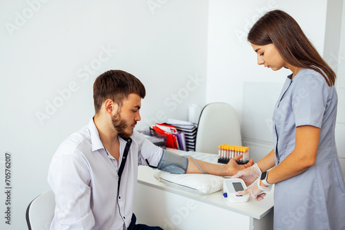 Nurse in medical uniform and transparent gloves checking blood pressure of young man in casual clothes.