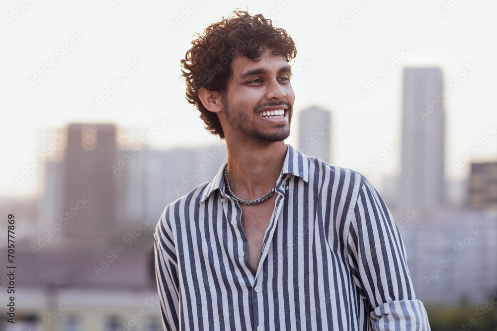 An attractive curly-haired guy in a striped shirt smiles against the backdrop - obrazy, fototapety, plakaty 