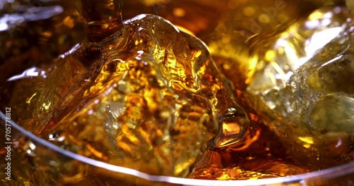 Super slow motion macro of old malt bourbon whiskey is poured in cocktail with ice cubes in transparent glass is being mixed by bartender in bar or club.