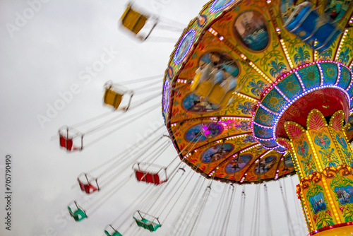 Detalhe de um brinquedo de rotação, grande e colorido, no parque de diversões com poucas pessoas, em um dia nublado.
