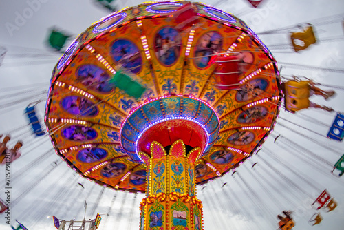 Um brinquedo gigante de rotação no parque de diversões com poucas pessoas, em um dia nublado. Foto feita de baixo para cima.