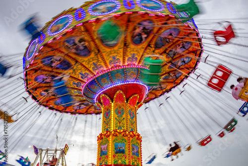 Um brinquedo gigante de rotação, com várias cadeiras no alto, borradas pela velocidade do movimento, no parque de diversões com poucas pessoas, em um dia nublado. Foto feita de baixo para cima.